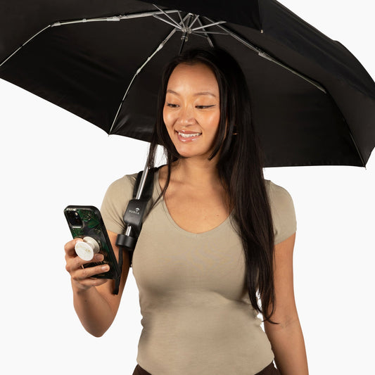 Woman holding a black umbrella with a visible brand logo, smiling and looking at her phone.